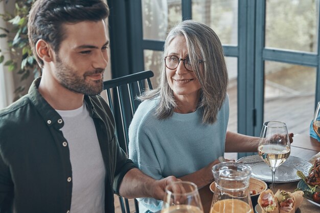 Feliz madre e hijo senior sonriendo mientras cenan juntos