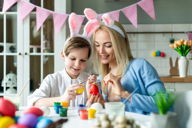 Feliz madre e hijo vistiendo en orejas de conejo preparándose para Pascua y pintando huevos. Primer retrato