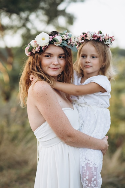 Feliz madre elegante y su hermosa hija con coronas de flores en un parque al atardecer