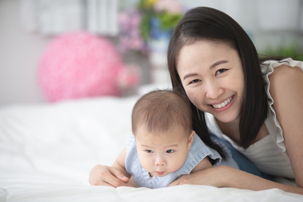 Feliz madre de familia asiática con hijo jugando en la cama con cara de sonrisa