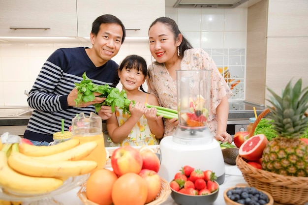 La feliz madre de familia asiática y su hija disfrutan preparando frutas recién exprimidas con verduras para hacer batidos para el desayuno juntos en la cocina. dieta y concepto de alimentos saludables.
