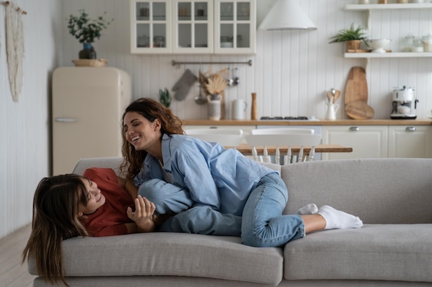 Feliz madre de familia e hija adolescente divirtiéndose riendo mientras se relajan juntos en el sofá en casa