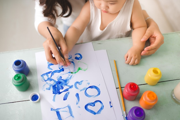 Foto feliz madre de familia e hija juntas pintan. la mujer asiática ayuda a su niña.