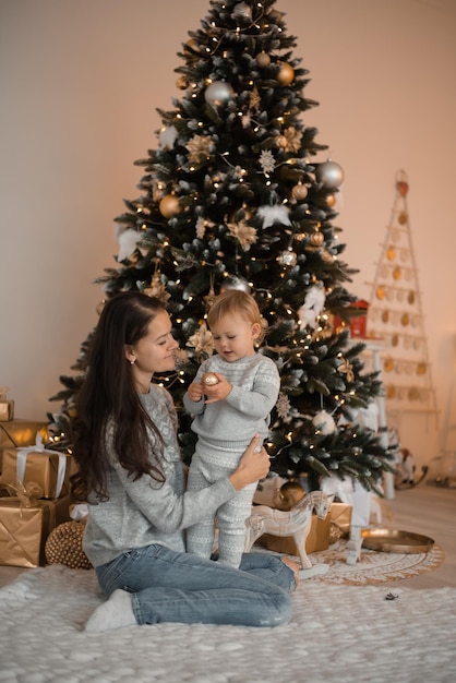 Feliz madre de familia e hija del niño cerca del árbol de Navidad en casa