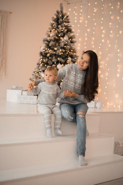 Feliz madre de familia e hija del niño cerca del árbol de Navidad en casa