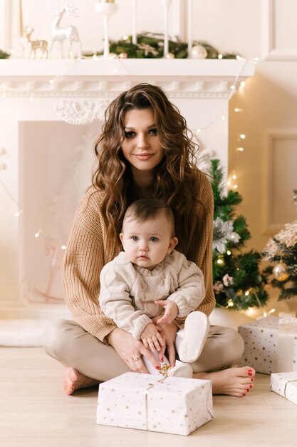 Feliz madre de familia e hija del niño en la mañana de Navidad en el árbol de Navidad con regalos