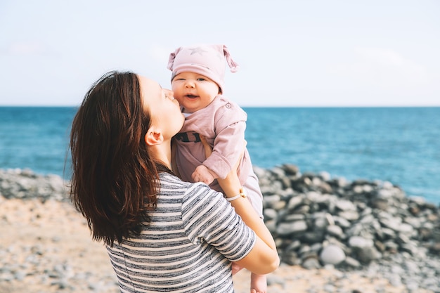 Feliz madre de familia joven y bebé jugando al aire libre en la playa del mar