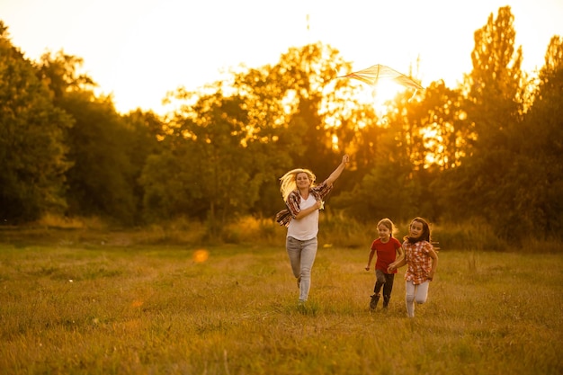 feliz madre de familia y niños corren en el prado con una cometa en el verano en la naturaleza