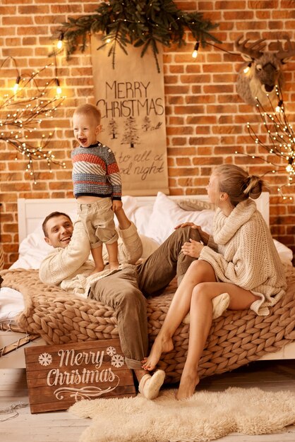 Feliz madre de familia, padre e hijo en la mañana de Navidad en el dormitorio jugando y divirtiéndose