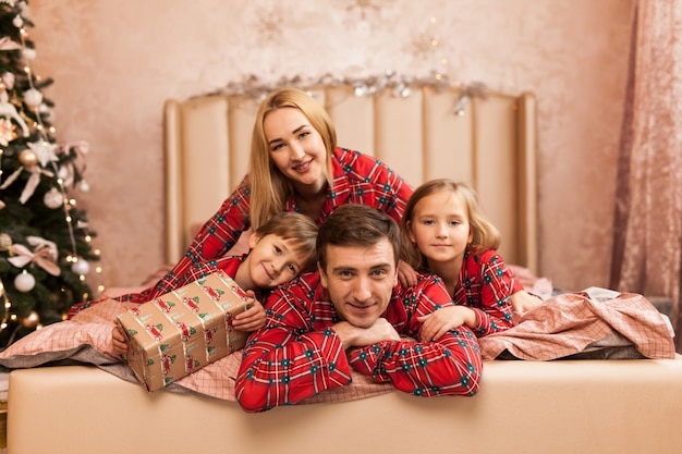 Feliz madre de familia, padre e hijos en la mañana de Navidad en la cama en pijama