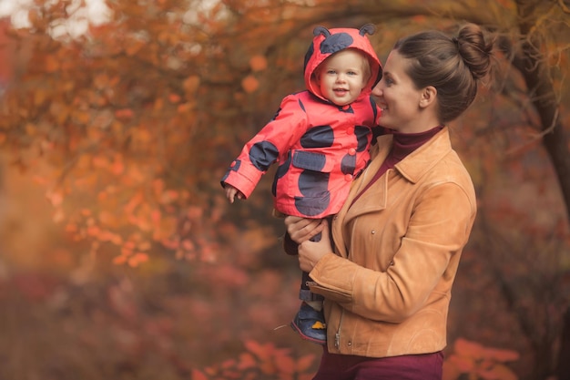 Feliz madre de familia y pequeña hija jugando en el parque natural de otoño