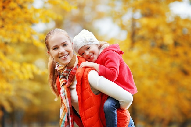 Feliz madre de familia y su pequeña hija juegan en el paseo de otoño en la naturaleza al aire libre