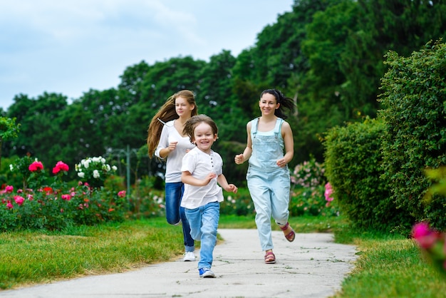 Feliz madre con hija e hijo corriendo sobre el césped sonriendo.