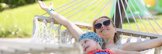 Feliz madre con hija yacía en una hamaca a la sombra disfruta de la vida y las vacaciones