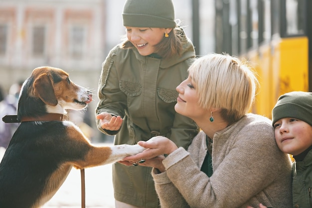 Feliz madre con hijos comunicarse con un perro en la calle.