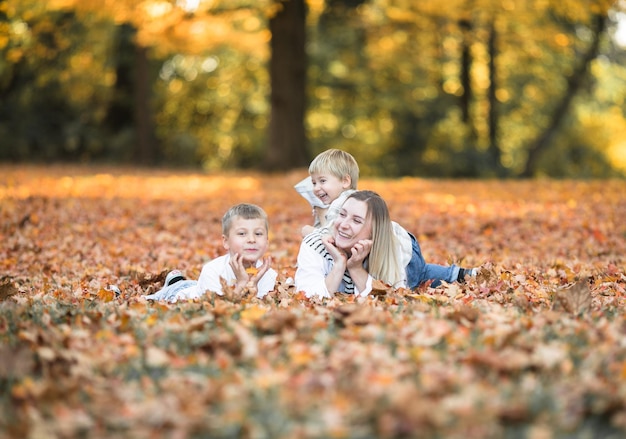 Feliz madre joven y dos hermanos caminando en el bosque de otoño