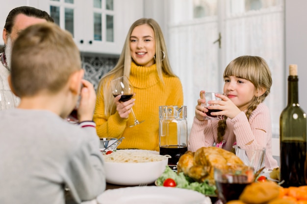 Feliz madre joven y linda hijita sosteniendo copas con bebidas en la mesa de vacaciones de acción de gracias