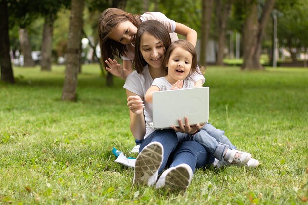 Feliz madre joven y pequeña hija sonriente sentada en la naturaleza y hablando por videollamada, vi divertido