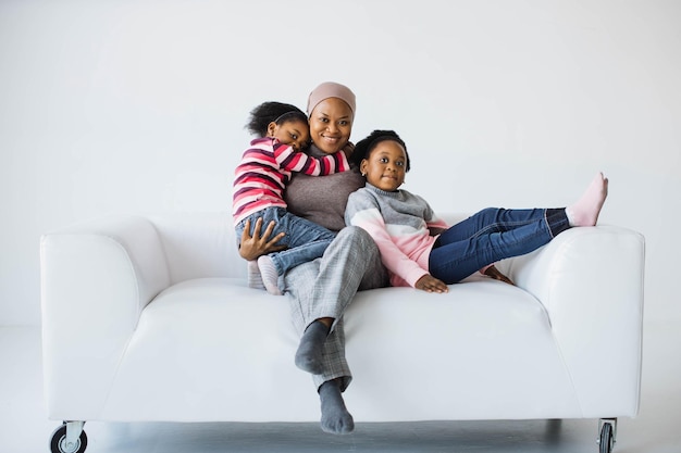 Feliz madre musulmana afroamericana descansando con sus hijas en el sofá