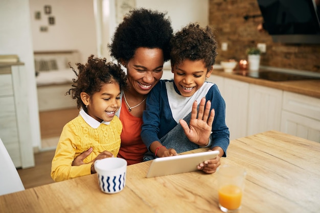 Feliz madre negra y sus hijos haciendo videollamadas a través del panel táctil en casa