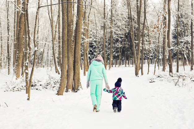 Feliz madre y niña en la caminata en el bosque nevado de invierno.