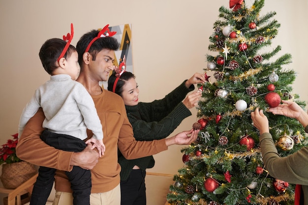 Feliz madre, padre e hijo pequeño decorando el árbol de Navidad en casa para las vacaciones de invierno