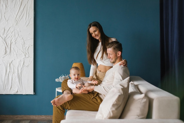 Feliz madre y padre de familia con un niño en casa en una habitación azul con un sofá blanco