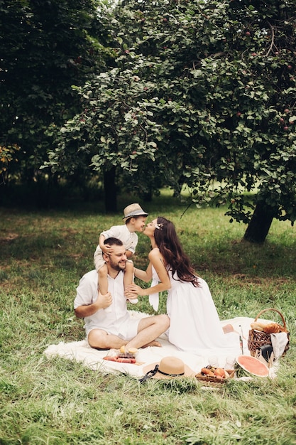 Feliz madre, padre y su lindo hijo pequeño haciendo un picnic en el parque de verano. Niño sentado sobre los hombros de su padre. Concepto de familia y ocio