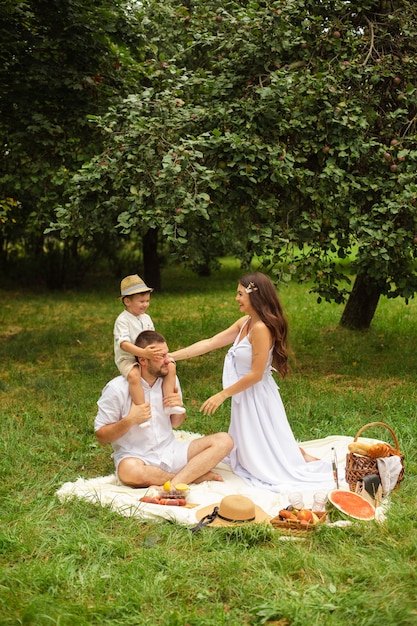 Feliz madre, padre y su lindo hijo pequeño haciendo un picnic en el parque de verano. Niño sentado sobre los hombros de su padre. Concepto de familia y ocio