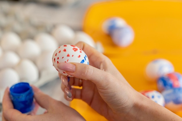 Feliz madre de Pascua sostiene huevo de Pascua pintado por su hija niño dibuja acuarelas azules y rojas en