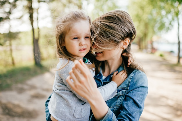 Feliz madre sonriente abrazando a su pequeña hija encantadora al aire libre