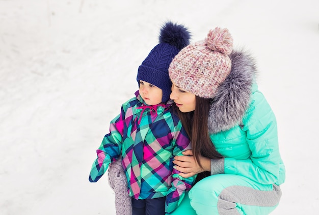 Feliz madre sosteniendo a la niña en el paseo en el bosque nevado de invierno