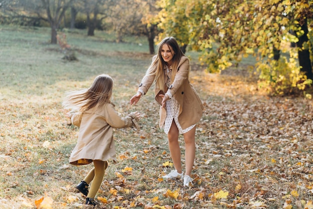 Feliz madre y su hermosa hija se divierten y caminan en el parque de otoño.