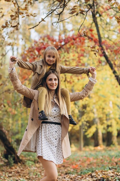 Feliz madre y su hermosa hija se divierten y caminan en el parque de otoño.