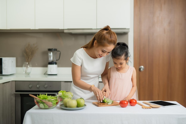 Feliz madre y su hija disfrutan haciendo y comiendo comida saludable juntos en su casa