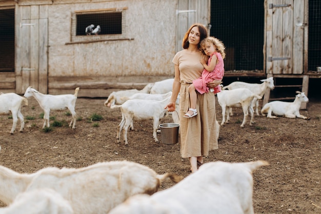 Feliz madre y su hija pasan tiempo en una granja ecológica entre cabras.