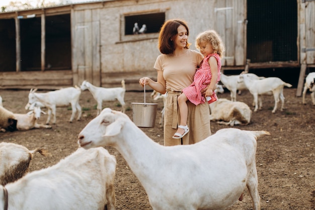 Feliz madre y su hija pasan tiempo en una granja ecológica entre cabras.