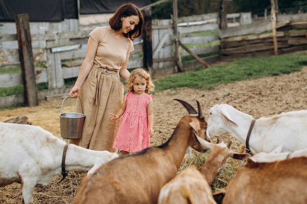 Feliz madre y su hija pasan tiempo en una granja ecológica entre cabras.