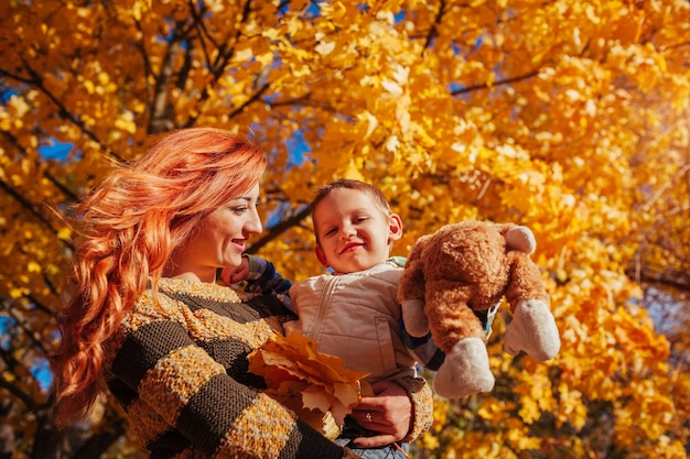 Feliz madre y su pequeño hijo caminando y divirtiéndose en el bosque de otoño. El niño está jugando con un juguete