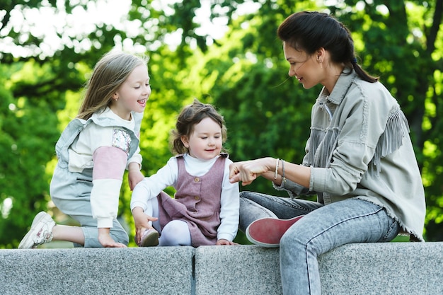 Feliz madre y sus dos hijas sentadas y jugando en un parque de la ciudad