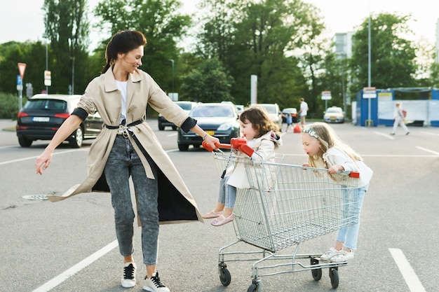 Feliz madre y sus hijas se divierten con un carrito de compras