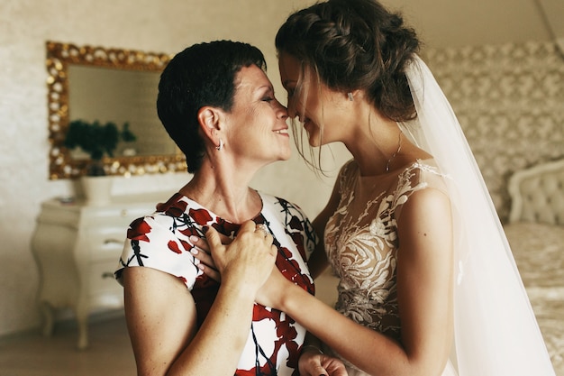 Feliz madre tiene la mano de la novia de pie con ella en la habitación