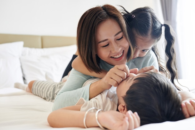 Feliz madre vietnamita jugando con su hija y su hijo en la cama