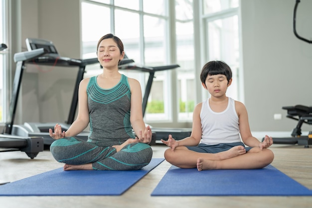 Feliz mãe asiática e filho vestindo roupas esportivas praticam ioga juntos em um pequeno clube esportivo de ginástica