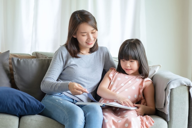 Feliz mãe asiática ensinando sua filha linda a estudar na sala de estar em casa