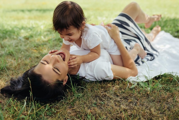 Feliz mãe caucasiana e sua filha brincando ao ar livre na grama depois do piquenique Mãe bonita e seu filho alegre se divertem no parque Retrato de família feliz Conceito de maternidade e infância