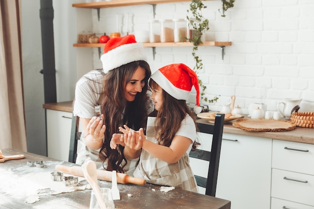 Feliz mãe e criança alegres com chapéus de Papai Noel estão cozinhando biscoitos de Natal na cozinha ano novo e Natal