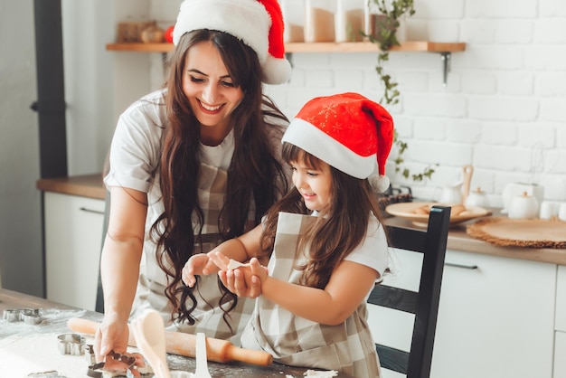 Feliz mãe e criança alegres com chapéus de Papai Noel estão cozinhando biscoitos de Natal na cozinha ano novo e Natal