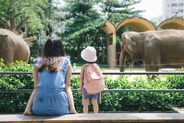 Feliz mãe e filha assistindo e alimentando elefantes no zoológico.