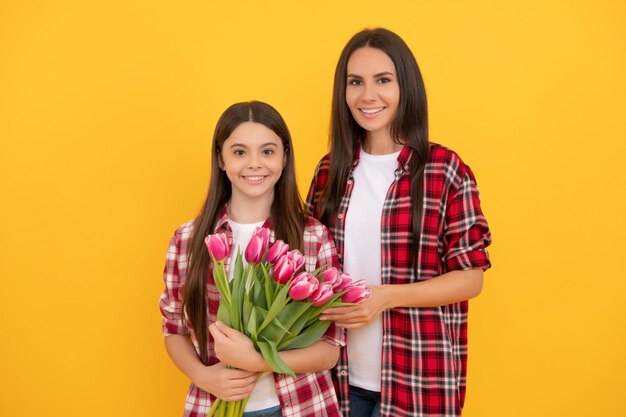 Feliz mãe e filha com flores de tulipa em fundo amarelo